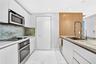 Modern kitchen featuring flat-panel white cabinetry, stone slab countertops, integrated stainless steel appliances, and wood-finish accent paneling wi