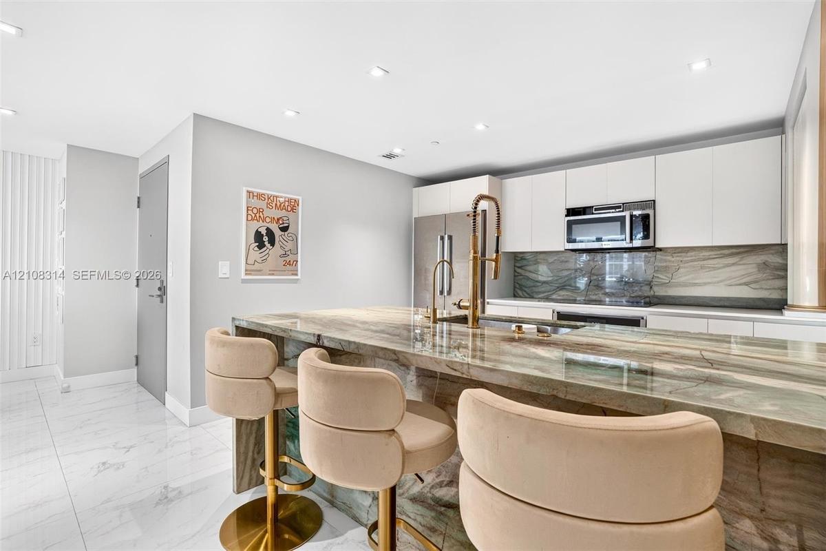 Kitchen featuring a stone waterfall island with a metal gooseneck faucet, white flat-panel cabinetry, a matching stone backsplash, stainless steel app