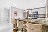 Kitchen featuring a stone waterfall island with a metal gooseneck faucet, white flat-panel cabinetry, a matching stone backsplash, stainless steel app