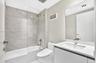 Bathroom featuring a vanity with a white countertop and integrated sink, frameless glass shower enclosure, stone-finish tile surround, and large wall-