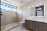 Bathroom featuring a walk-in shower with large-format tile surround, frameless glass enclosure, a wood-finish vanity with a stone countertop, and an i