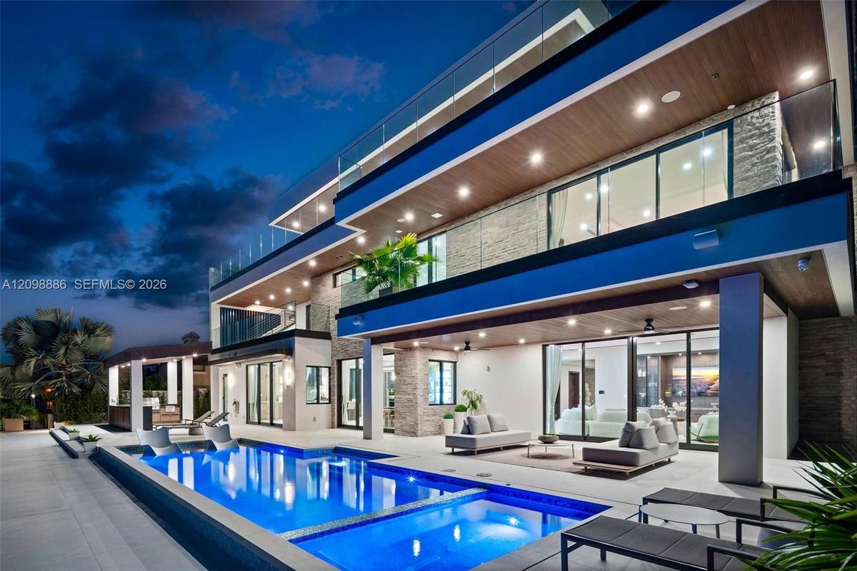 Contemporary multi-level exterior featuring stacked stone masonry, recessed soffit lighting, glass panel balcony railings, and a heated pool with an i