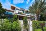 Modern multi-level exterior featuring white stucco facade, dark wood-finish soffits, integrated glass balcony railings, stone cladding accents, and ho