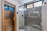 Built-in wood-paneled sauna featuring a glass-door entrance, accompanied by a walk-in shower with a mosaic-tiled accent wall, glass enclosure, transom
