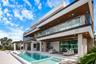 Contemporary multi-level exterior featuring stacked stone masonry, a glass-railed balcony, deep recessed wood-finish soffits, and a rectangular swimmi