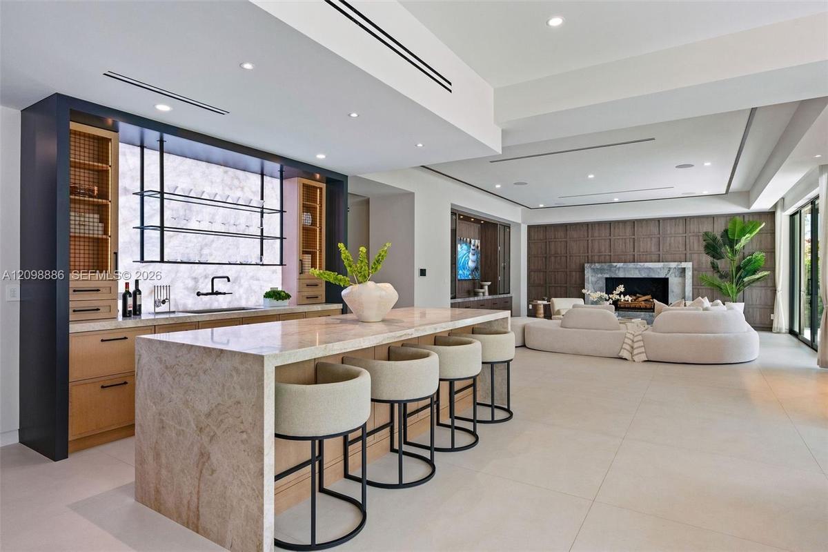 Stone-topped kitchen island with bar seating, custom cabinetry featuring integrated shelving, recessed lighting, and floor-to-ceiling wood wall paneli