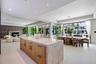 Large kitchen island featuring a waterfall stone countertop and light wood-finish cabinetry with matte black hardware, stone tile flooring, a floor-to