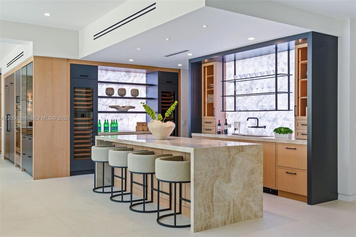 Kitchen featuring a waterfall-edge stone island, built-in dual wine refrigeration, stone slab backsplash, recessed ceiling lighting, and custom cabine