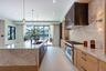 Kitchen featuring custom wood cabinetry, natural stone countertops and backsplash, professional-grade range, custom metal range hood, and large center