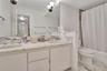 Dual-sink vanity with stone-finish countertop and backsplash, wall-to-wall mirror, brushed metal hardware, and tub-shower combination with floor-to-ce