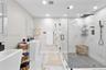 Bathroom featuring large-format stone-finish flooring, pedestal sinks, and a walk-in glass-enclosed shower with contrasting hexagon tile flooring, sto