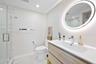 Bathroom featuring a wall-mounted vanity with wood-finish cabinetry, an integrated sink with a chrome faucet, a backlit oval mirror, and a walk-in gla