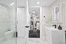 Modern bathroom featuring a tall white pedestal sink with matte black hardware, a glass-enclosed shower, built-in cabinetry, and white tile flooring w
