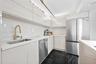 Kitchen featuring high-gloss cabinetry, stone-surface countertops, full-height stone backsplash, stainless steel appliances, and dark-toned flooring w