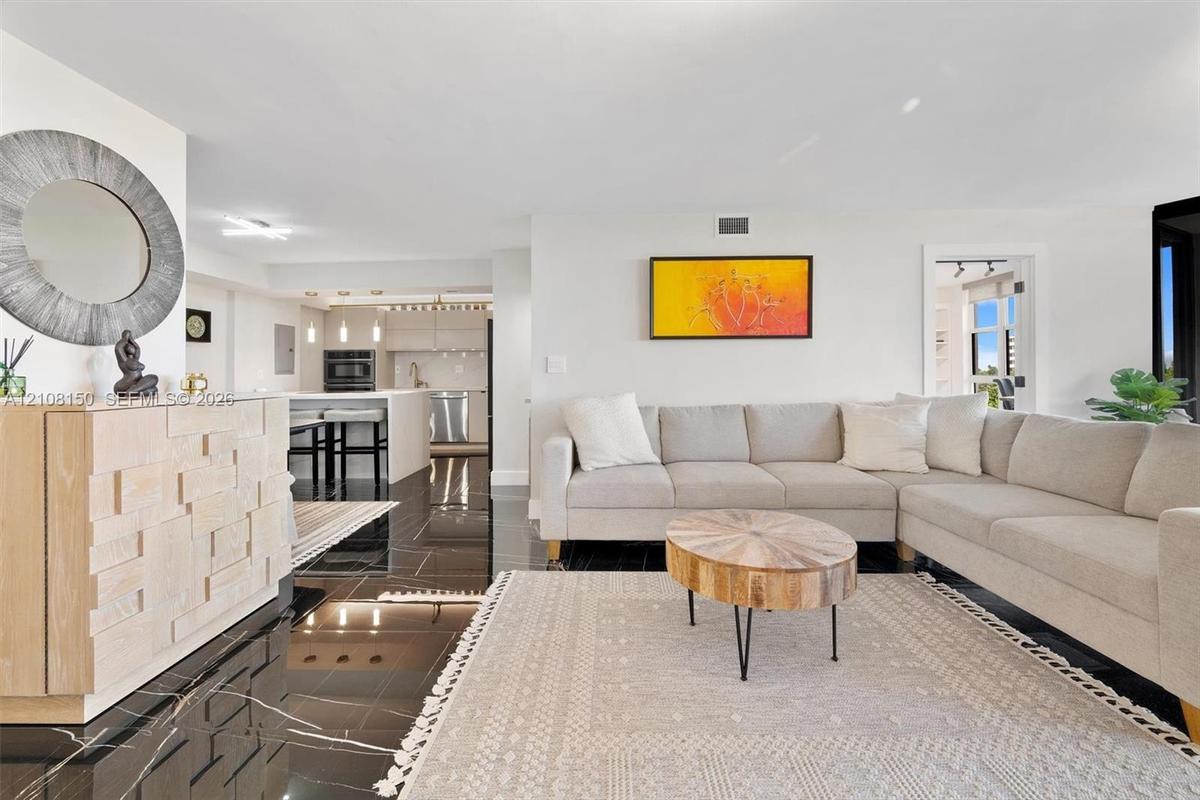 Open-concept interior featuring large-format polished dark stone flooring, recessed lighting, and kitchen cabinetry with integrated stainless steel ap