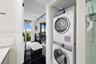 Stacked front-load laundry unit, black polished flooring with white veining, floor-to-ceiling windows, and track lighting