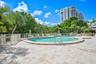 Outdoor pool area featuring a stone-paver deck, metal safety fencing, and mature landscaping