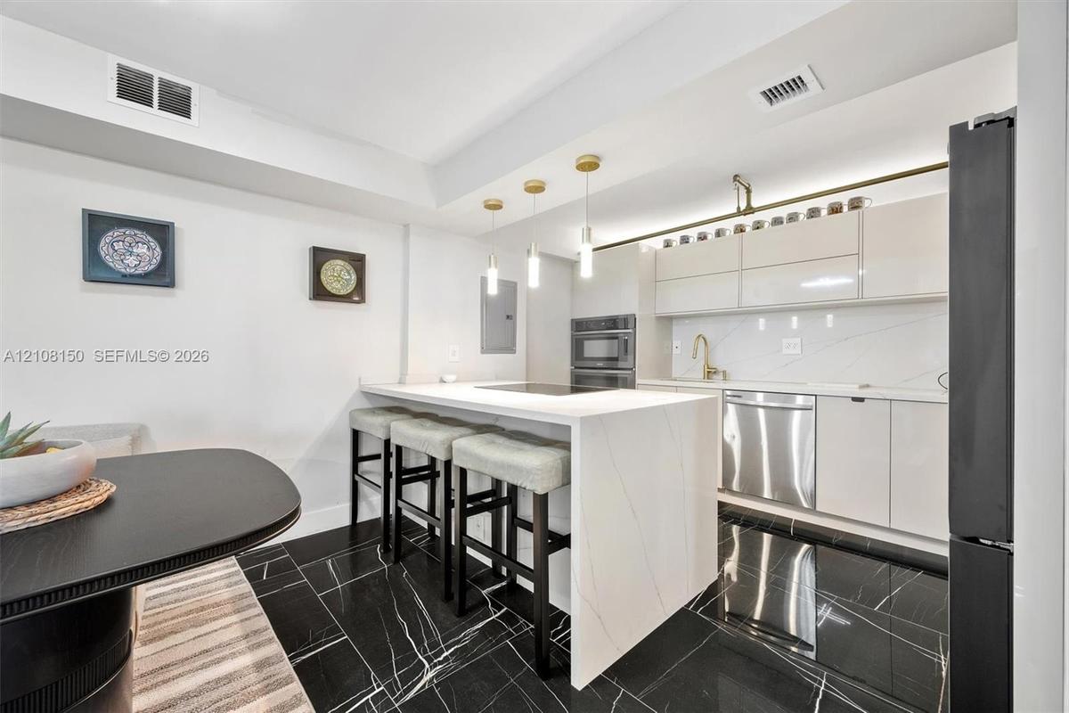 Kitchen featuring an island with a stone-finish waterfall edge, high-gloss cabinetry, stainless steel appliances, pendant lighting, and polished stone