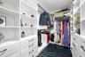 Custom walk-in closet featuring white built-in shelving, floor-to-ceiling storage units, multiple drawers with matte black hardware, integrated hangin
