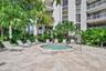 Outdoor spa featuring a stone-tile surround, light-toned paved deck, metal handrail, and tropical landscaping