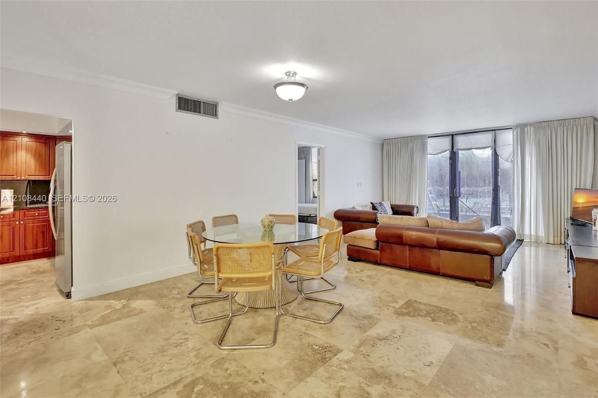 Open-concept living space featuring polished stone flooring, ceiling-mounted light fixtures, crown molding, and floor-to-ceiling glass panel doors