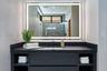 Dark wood vanity featuring integrated open shelving, a dark solid-surface countertop, an undermount rectangular sink, and a matte black faucet paired 