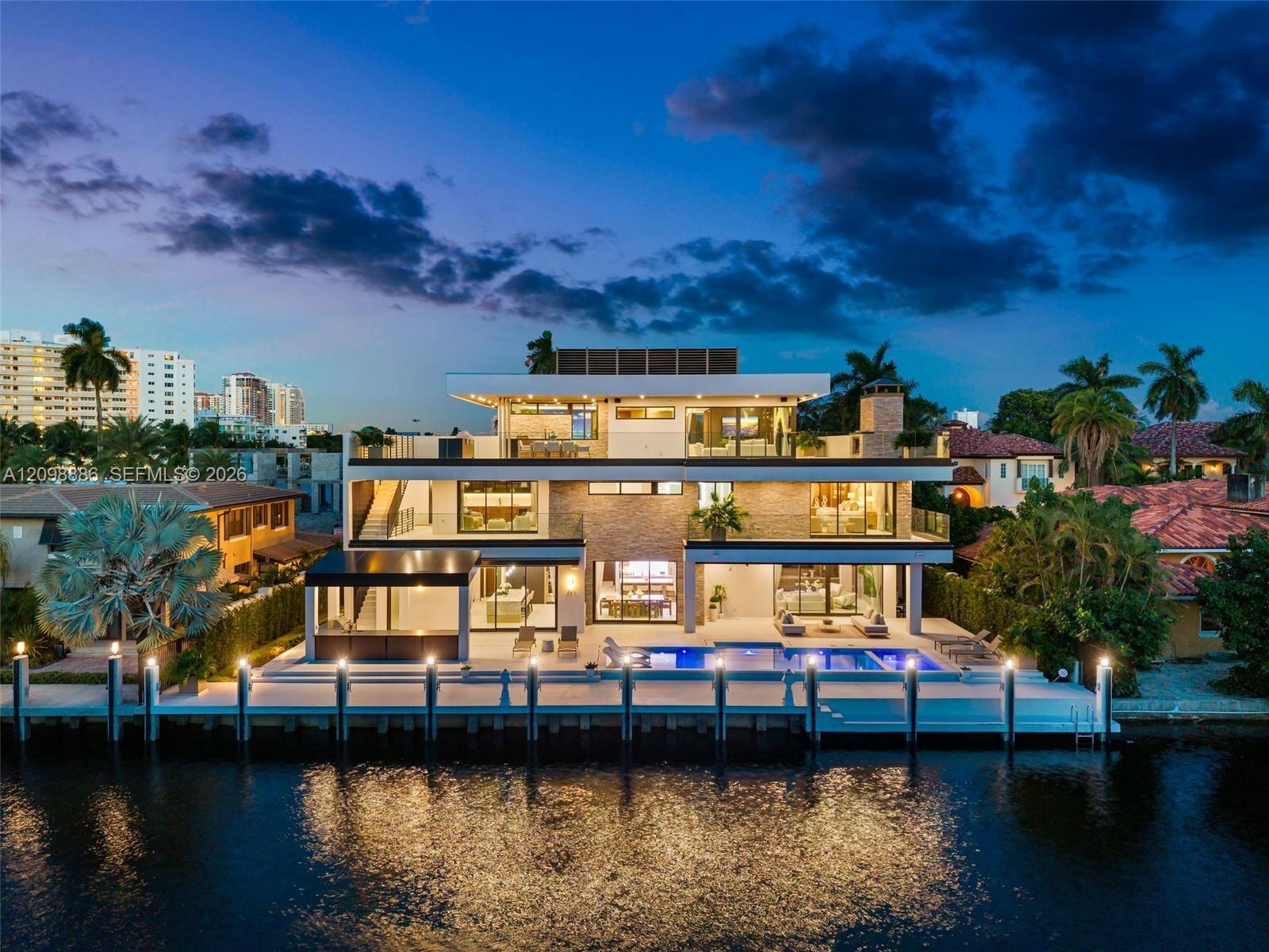 Three-story modern waterfront residence featuring a private boat dock, multi-level terraces with glass railings, stone veneer accents, and a rectangul