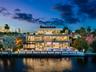 Three-story modern waterfront residence featuring a private boat dock, multi-level terraces with glass railings, stone veneer accents, and a rectangul