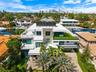 Multi-level contemporary residence featuring a flat roofline, glass panel balcony railings, stone-paved driveway, elevated terrace with turf surfacing