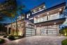 Contemporary multi-level exterior featuring stacked stone masonry, horizontal glass panel garage doors, glass-railed balconies, and wood-finish soffit