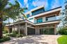 Modern multi-level exterior featuring stacked stone masonry, horizontal glass panel garage doors, glass balcony railings, and wood-finish soffits