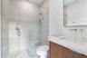 Walk-in shower featuring textured wall tile, glass enclosure, and rainfall showerhead, paired with a wood-finish vanity, solid-surface countertop, and