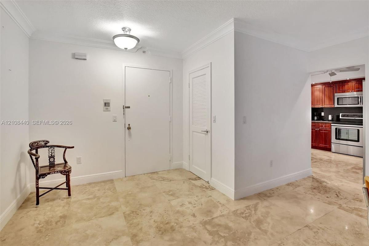 Neutral-tone tile flooring, crown molding, semi-flush mount ceiling light, and louvered-panel door