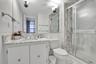 Bathroom featuring a stone-surface vanity with an integrated sink, floor-to-ceiling stone-tiled shower enclosure, chrome-finish sliding glass shower d