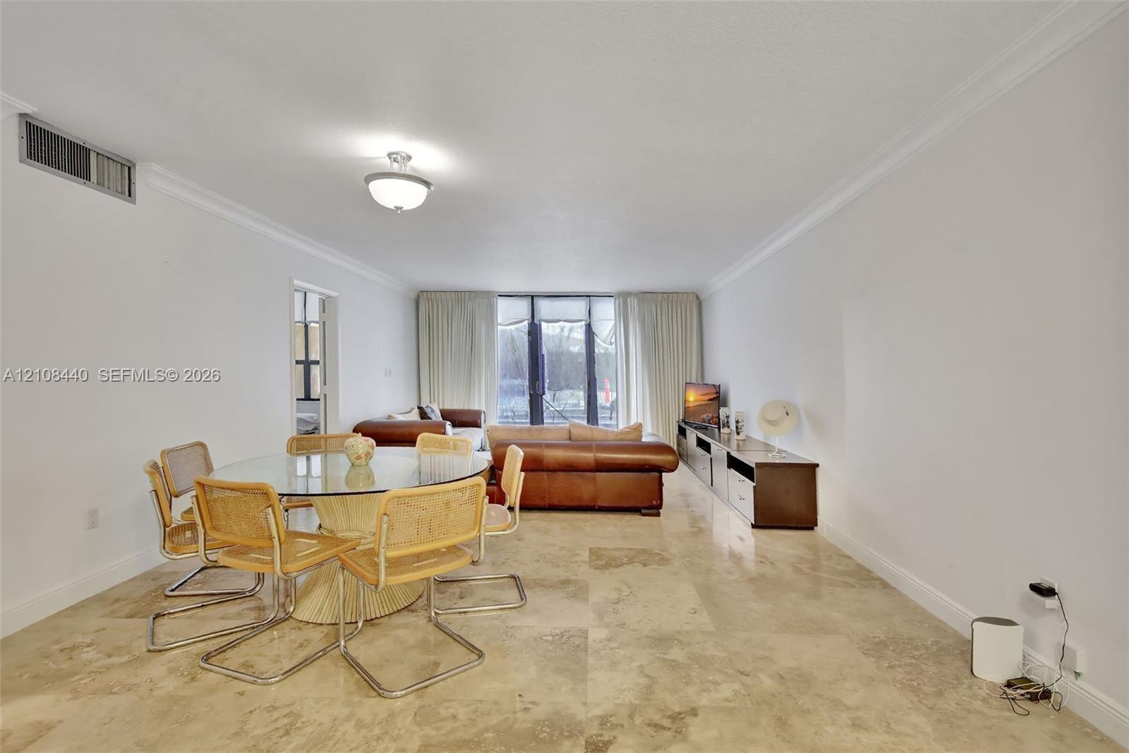 Open-concept interior featuring large-format stone flooring, crown molding, and floor-to-ceiling glass panel doors