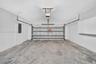 Two-car garage featuring a concrete floor, motorized sectional garage door, white wall-mounted storage cabinetry, and an electrical service panel