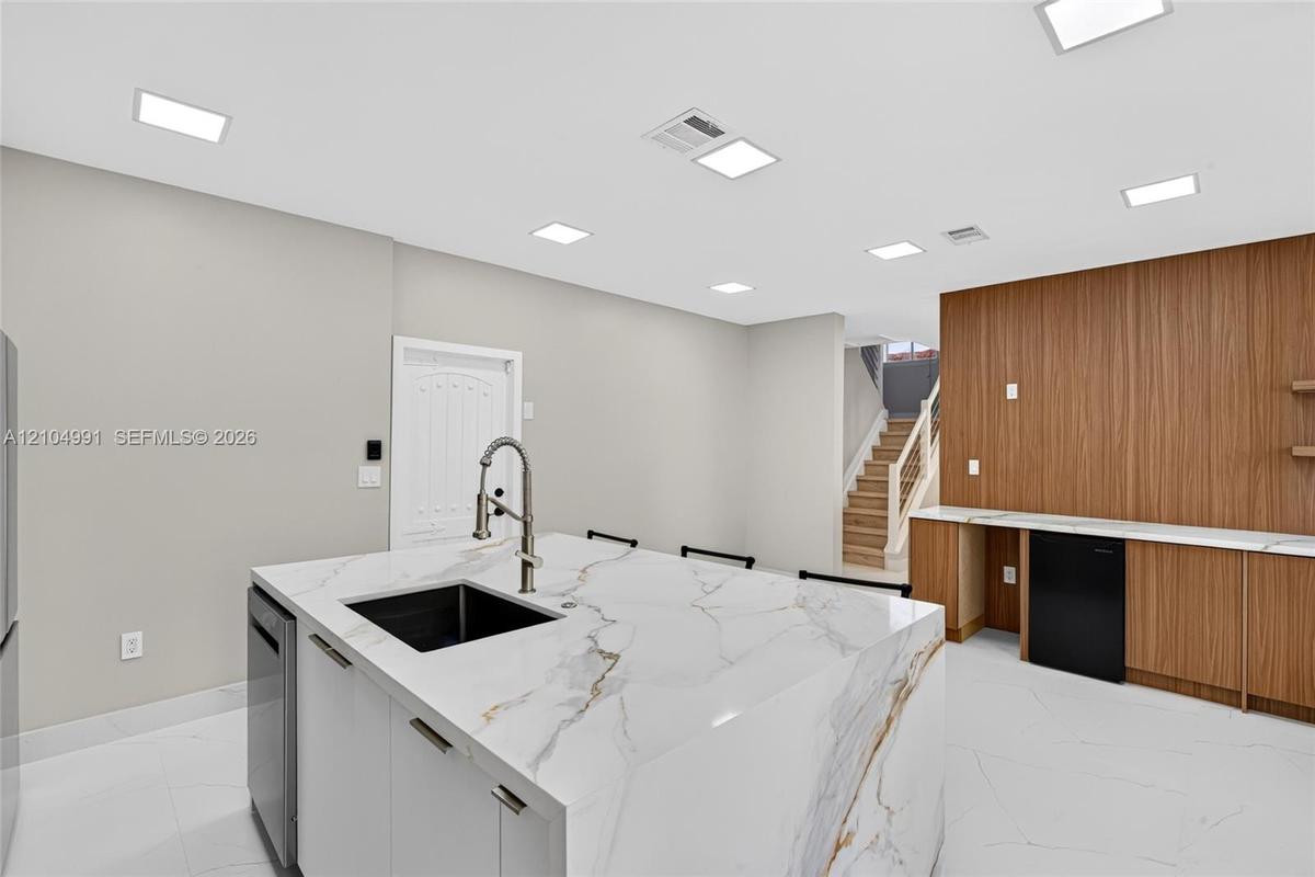 Kitchen island with stone-finish waterfall countertop and undermount sink, recessed lighting, wood-finish wall paneling, built-in cabinetry, and tile 
