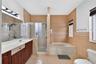 Bathroom featuring a dual-sink wood-finish vanity with an integrated countertop, a glass-enclosed shower, a deep soaking tub, and tile wall surrounds