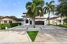 Two-story exterior featuring a clay tile roof, arched entryway, multi-panel garage door, and a geometric concrete paver driveway with turf accents