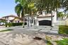 Two-story exterior featuring white stucco finish, arched entryways, multi-car garage with dark metal doors, tile roof, and a paved driveway with integ
