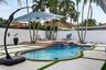 Backyard featuring a custom-shaped swimming pool with a tiered tile spa, concrete paver patio with turf detailing, and a perimeter privacy fence
