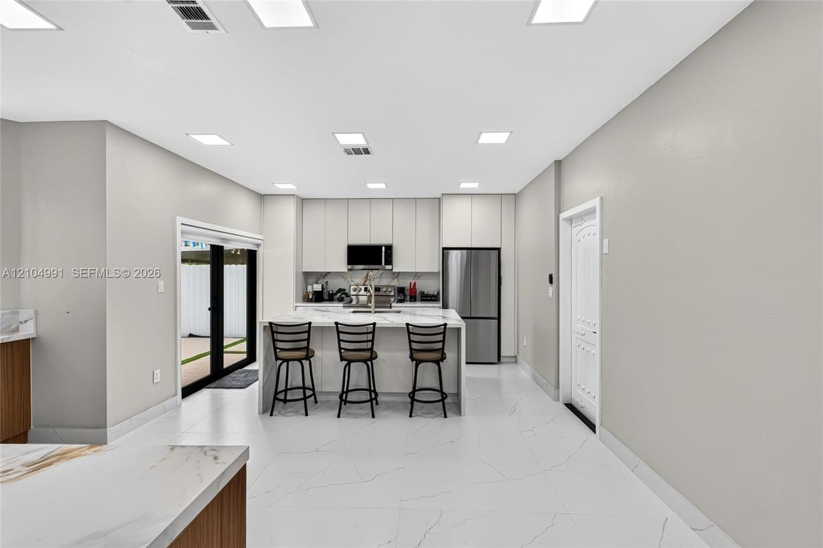 Kitchen featuring floor-to-ceiling cabinetry, a central island with a stone-surface countertop, stainless steel appliances, and large-format tile floo