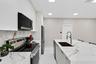 Kitchen featuring white slab cabinetry, large-format tiled flooring, stone-finish countertops with matching full-height backsplash, stainless steel ap