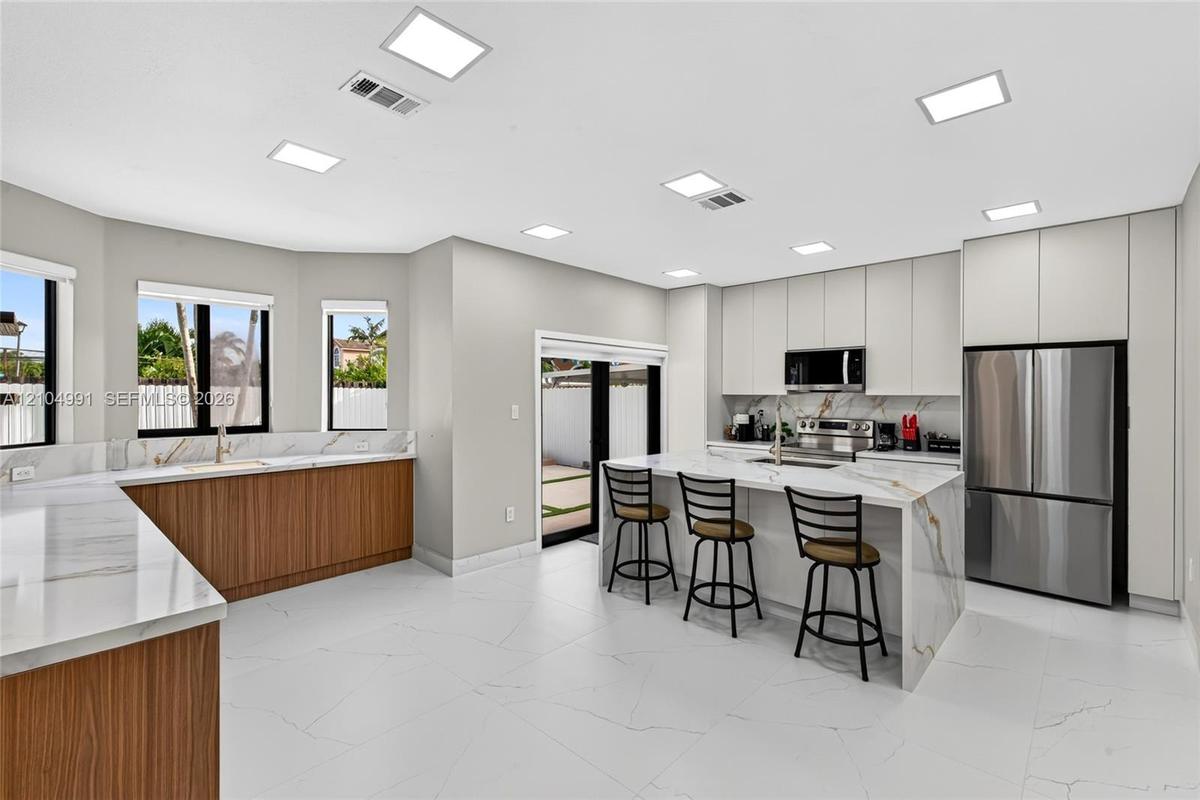 Modern kitchen featuring flat-panel cabinetry, stone-finish countertops with waterfall edge, stainless steel appliances, and large-format tile floorin