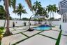 Outdoor living area featuring a swimming pool with a raised spa, concrete paver patio with turf inlays, privacy fencing, and mature palm trees