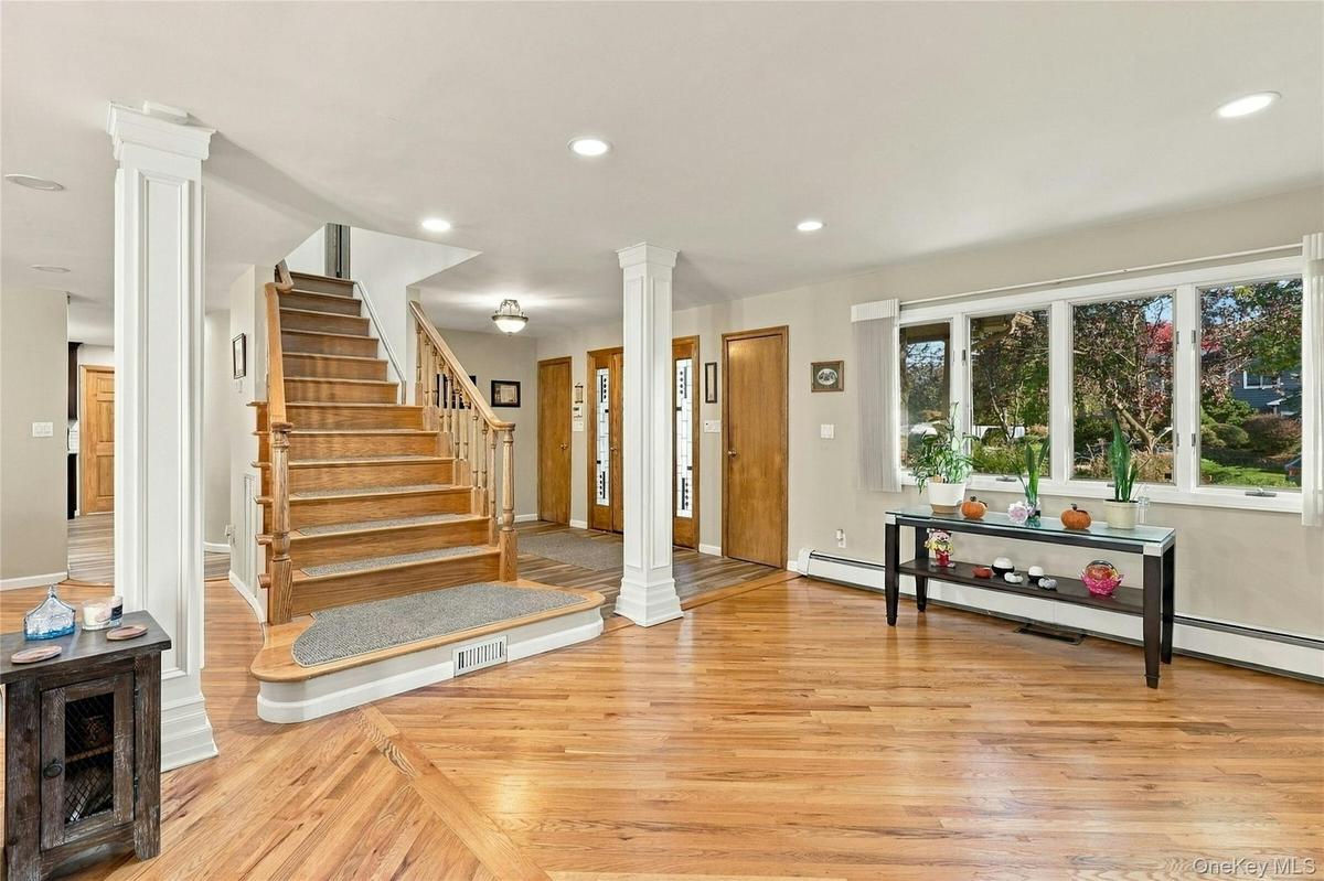 Open-concept interior featuring wood-finish flooring, a central staircase with a wood-finish handrail, architectural columns, multiple wood-finish int