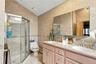 Bathroom featuring a double-sink vanity with a solid-surface countertop, tiled wall surfaces, and a glass-enclosed shower