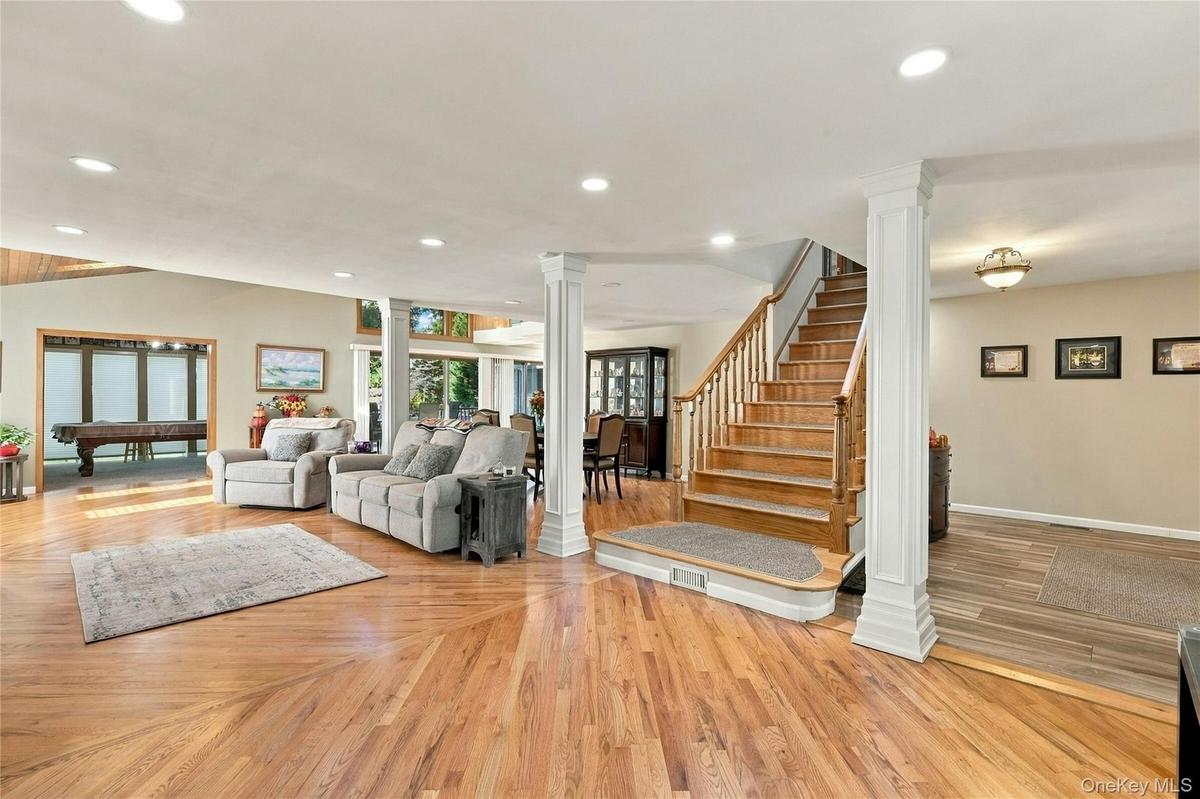 Open-concept interior featuring wood-finish flooring, recessed lighting, decorative white columns, and a wooden staircase with a matching handrail
