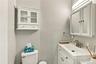 White vanity with integrated rectangular sink and metallic faucet, complemented by a mirrored medicine cabinet, wall-mounted light fixture, and white 