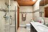 Bathroom featuring a walk-in shower with glass enclosure, wood-paneled ceiling, stone-finish wall tile with mosaic accent inlay, and vanity with stone